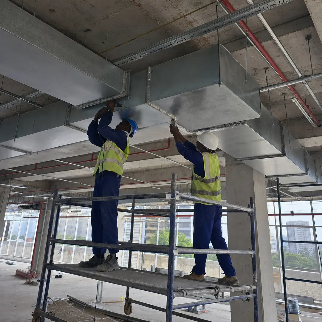Two technicians installing rectangular galvanised supply ductwork in a high-rise office fit-out.